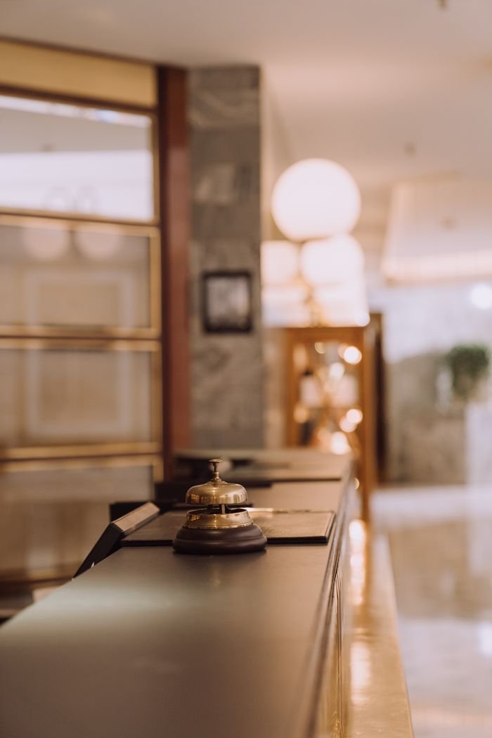 about-us-02 A close-up view of a hotel reception counter with a classic bell and warm lighting.