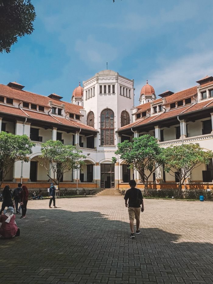 services-03 The iconic Lawang Sewu building with people walking in its courtyard under a bright blue sky.